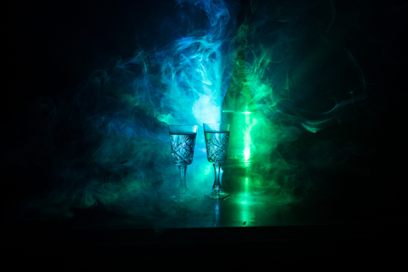 Two glasses of Vodka with bottle on dark foggy club style background with glowing lights (Laser, Stobe) Multi colored. Club drinks theme decoration. Empty space. Selective focusの写真素材
