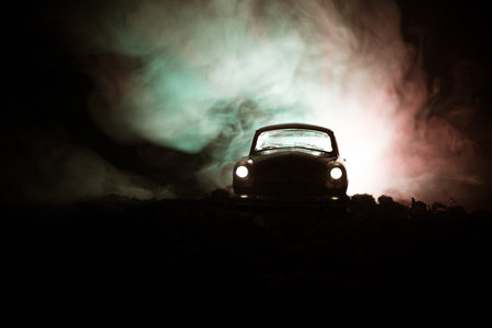 Silhouette of old vintage car in dark foggy toned background with glowing lights in low light, or silhouette of old crime car dark background. Selective focusの写真素材