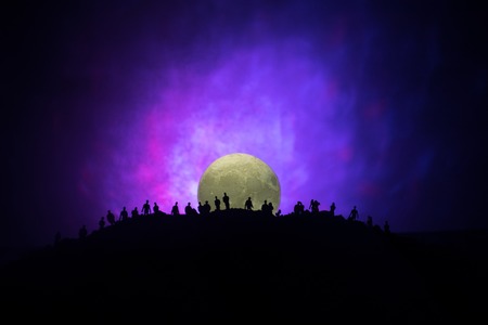 Scary view crowd of zombies on hill with spooky cloudy sky with fog and rising full moon. Silhouette group of zombie walking under full moon. Halloween concept.の写真素材