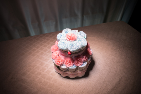 Cake of diapers, baby shower gift diaper, wrapped diapers, a roll of diapers, wrapped a clean diaper on table with baby doll decorated. Selective focus. Newborn greeting card or giftの写真素材
