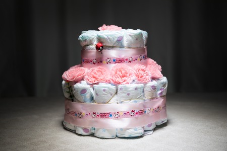 Cake of diapers, baby shower gift diaper, wrapped diapers, a roll of diapers, wrapped a clean diaper on table with baby doll decorated. Selective focus. Newborn greeting card or giftの写真素材