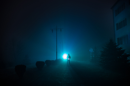 Night Landscape. City at night in dense fog. Mystical landscape surreal lights with creepy man. The walking man's silhouette in night fog at artificial light.の写真素材