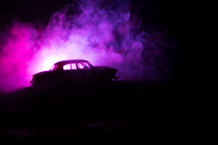 Silhouette of old vintage car in dark foggy toned background with glowing lights in low light, or silhouette of old crime car dark background. Selective focusの写真素材