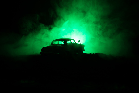 Silhouette of old vintage car in dark foggy toned background with glowing lights in low light, or silhouette of old crime car dark background. Selective focusの写真素材