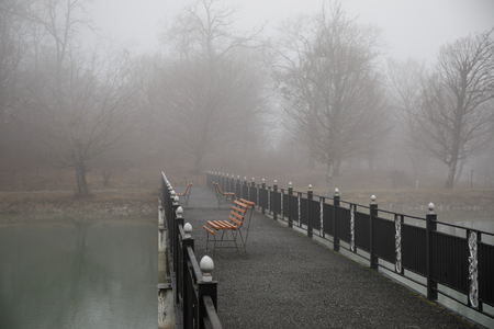 Amazing landscape of bridge reflect on surface water of lake, fog evaporate from pond make romantic scene or Beautiful bridge on lake with trees at fog. Iron bridge over lake in misty morning.の写真素材