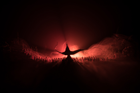 Lamp of wishes. Silhouette of a large crowd of people standing against a big lamp of wishes with toned light beams on foggy background. Dark night table decoration. Selective focusの写真素材