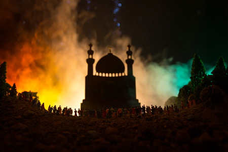 Silhouette of a large crowd of people in forest at night standing against a blurred mosque building with toned light beams on foggy background. Ramadan Kareem background. Praying people concept.の写真素材