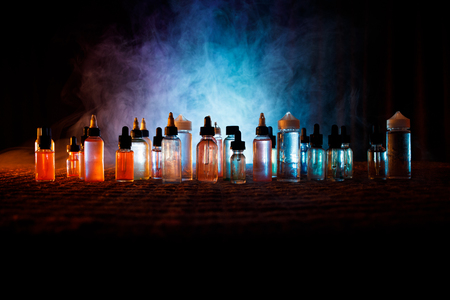 Vape concept. Smoke clouds and vape liquid bottles on dark background. Light effects. Useful as background or vape advertisement or vape background. Selective focusの写真素材