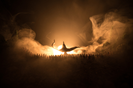 Lamp of wishes. Silhouette of a large crowd of people standing against a big lamp of wishes with toned light beams on foggy background. Dark night table decoration. Selective focusの写真素材