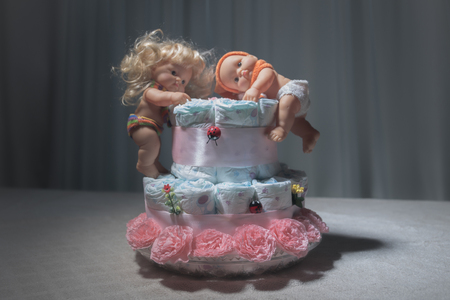 Newborn gift concept. Cake of diapers. Wrapped diapers as cake with flowers. Cake of wrapped clean diaper on table with baby doll decorated. Selective focus.の写真素材