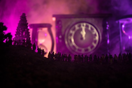 Silhouette of a large crowd of people in forest at night standing against a big arrow clock with...