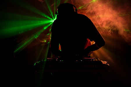 DJ Spinning, Mixing, and Scratching in a Night Club, Hands of dj tweak various track controls on dj's deck, strobe lights and fog, or Dj mixes the track in the nightclub at party. Selective focusの写真素材