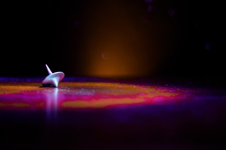 Totem spinning top spinning, wobbling and stopping. Spinning top on mirror surface with toned smoke background light. Whirligig in action in dark room on table. Selective focusの写真素材