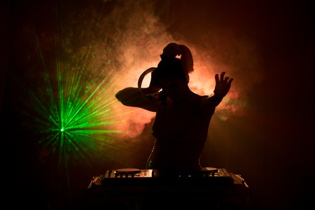 DJ Spinning, Mixing, and Scratching in a Night Club, Hands of dj tweak various track controls on dj's deck, strobe lights and fog, or Dj mixes the track in the nightclub at party. Selective focusの写真素材