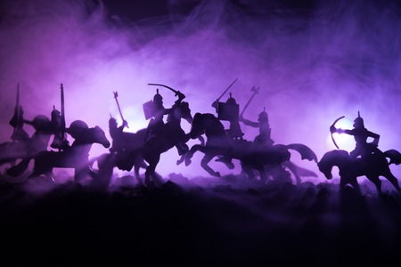 Medieval battle scene with cavalry and infantry. Silhouettes of figures as separate objects, fight between warriors on dark toned foggy background. Night scene. Selective focusの写真素材