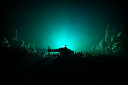 Military helicopter ready to fly from conflict zone or Silhouettes of a large crowd of people trying to escape with helicopter. Decorated night installed photo with foggy toned backlitの写真素材
