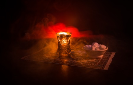 Eastern tea in traditional glasse and pot on black background with lights and smoke. Eastern tea concept. Armudu traditional Azerbaijan/Turkish cup. Selective focus. Glass of Teaの写真素材