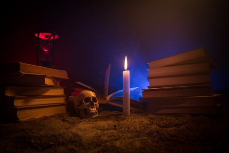 Wizard's Desk. A desk lit by candle light. A human skull, old books on sand surface. Halloween still-life background with a different elements on dark toned foggy background. Selective focusの写真素材