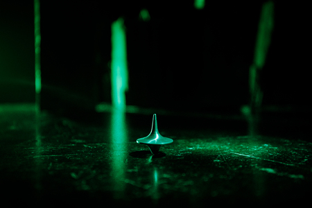 Totem spinning top spinning, wobbling and stopping. Spinning top on mirror surface with toned smoke background light. Whirligig in action in dark room on table. Selective focusの写真素材