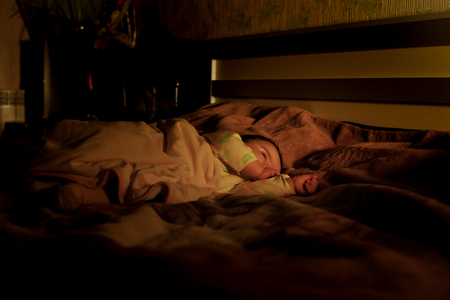 Child sleeping and dreaming in parents bed in dark yellow calm light. Selective focus. Cute little girl is sweetly sleeping in bed. Image with selective focus and toningの写真素材
