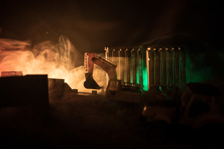 Construction site on a city street. A yellow digger excavator parked during the night on a construction site. Industrial concept table decoration on dark foggy toned background. Selective focusの写真素材