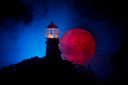 Lighthouse with light beam at night with fog. Old lighthouse standing on mountain. Table decoration. Toned background. Moonlighting. Selective focusの写真素材