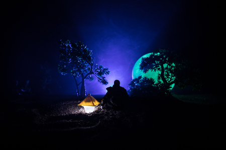 Man in raincoat coming from dark forest with glowing lantern in his hand concept. Silhouette of a horror killer with lamp. Decorationの写真素材