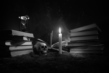 Wizard's Desk. A desk lit by candle light. A human skull, old books on sand surface. Halloween still-life background with a different elements on dark toned foggy background. Selective focusの写真素材