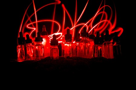 Vape concept. Smoke clouds and vape liquid bottles on dark background. Light effects. Useful as...