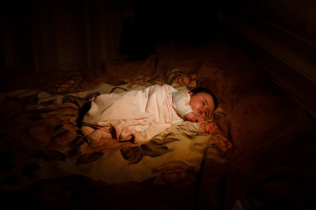 Child sleeping and dreaming in parents bed in dark yellow calm light. Selective focus. Cute little girl is sweetly sleeping in bed. Image with selective focus and toningの写真素材