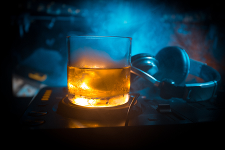Glass with whisky with ice cube inside on dj controller at nightclub. Dj Console with club drink at music party in nightclub with disco lights. Selective focusの写真素材