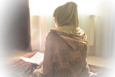 Muslim woman praying for Allah muslim god at room near window. Hands of muslim woman on the carpet praying in traditional wearing clothes, Woman in Hijab, Carpet of Kaaba, Selective focusの写真素材