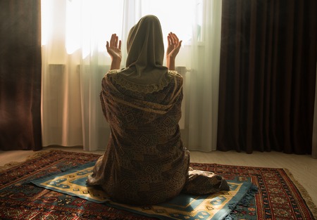 Muslim woman praying for Allah muslim god at room near window. Hands of muslim woman on the carpet praying in traditional wearing clothes, Woman in Hijab, Carpet of Kaaba, Selective focusの写真素材