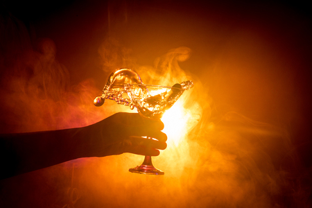 Martini cocktail glass in hand splashing on dark toned smoky background or colorful cocktail in glass with splashes and olives. Party club entertainment. Mixed light. Selective focusの写真素材