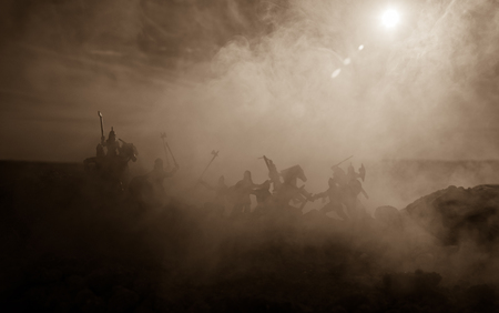 Medieval battle scene with cavalry and infantry. Silhouettes of figures as separate objects, fight between warriors on sunset foggy background. Selective focusの写真素材