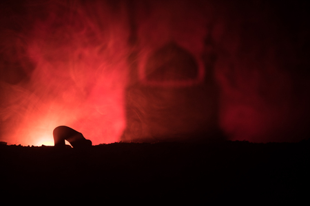 Silhouette of praying man with blurred mosque building on toned foggy background. Ramadan Kareem background. Muslim Eid holiday decoration. Praying people religion concept. Selective focusの写真素材