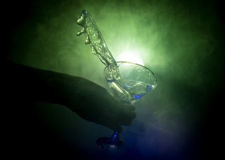 Martini cocktail glass in hand splashing on dark toned smoky background or colorful cocktail in glass with splashes and olives. Party club entertainment. Mixed light. Selective focusの写真素材
