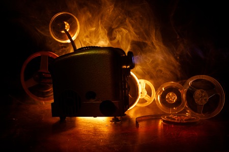 Old style movie projector, still-life, close-up. Film projector on a wooden background with dramatic lighting and selective focus. Movies and entertainment conceptの写真素材