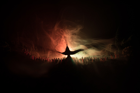 Lamp of wishes. Silhouette of a large crowd of people standing against a big lamp of wishes with toned light beams on foggy background. Dark night table decoration. Selective focusの写真素材