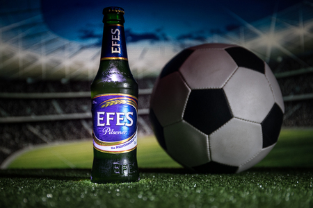 BAKU,AZERBAIJAN - JUNE 15, 2018 : Creative concept. Bottle of Efes Pilsner beer on grass with soccer ball and blurred stadium on background. Efes Pilsener is the flagship product of this companyのeditorial素材