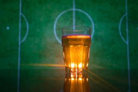 Creative concept. Pint of fresh beer on grass with blurred stadium on background with fog and light. Glass of lager beer ready for drink. Copy space. Selective focusの写真素材