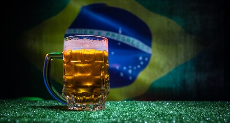 Creative concept. Pint of fresh beer on grass with blurred flag of Brazil on background or Glass of lager beer ready for drink. Copy space. Selective focusの写真素材