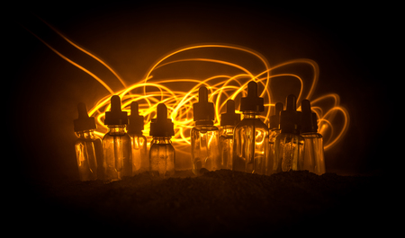 Vape concept. Smoke clouds and vape liquid bottles on dark background. Light effects. Useful as background or vape advertisement or vape background. Selective focusの写真素材