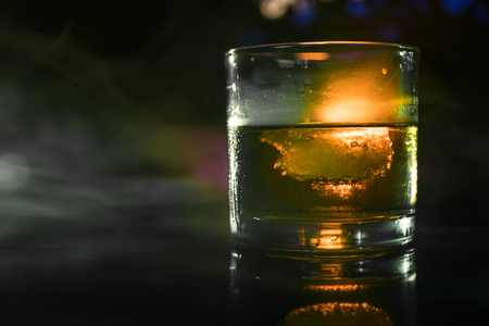 Selective focus pure whisky with ice cube inside whisky glass on dark foggy background alcohol drink concept. Close upの写真素材