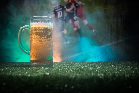 Creative concept. Pint of fresh beer on grass with blurred stadium on background with fog and light. Glass of lager beer ready for drink. Copy space. Selective focusの写真素材