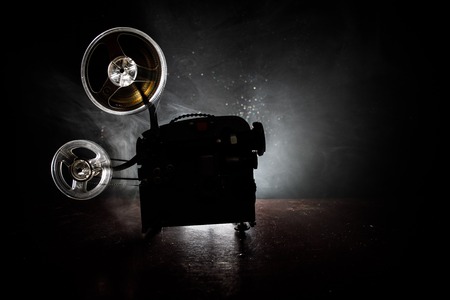 Old style movie projector, still-life, close-up. Film projector on a wooden background with dramatic lighting and selective focus. Movies and entertainment conceptの写真素材