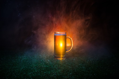 Creative concept. Single beer glass on green grass at dark toned foggy background. Watch football (soccer) with beer concept. Selective focusの写真素材