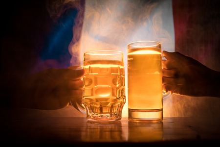Two friends toasting (clinking) with glasses of light beer at the pub. Beautiful background with blurred view of flag of France. Support your country with beer concept. Selective focusの写真素材