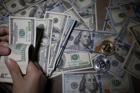 Hand counting US dollars with Bitcoin (New virtual money) coin over a lot of money close up selective focus. Digital Money and Bitcoin Concept.の写真素材