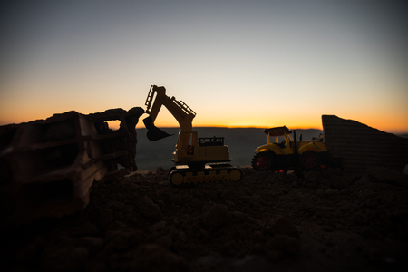 Construction site on a city street. A yellow digger excavator parked during the night on a construction site. Industrial concept table decoration on dark foggy toned background. Selective focusの写真素材